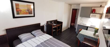 Une chambre d’hôtel de taille réduite, comprenant un lit, un bureau et une kitchenette.