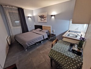 A compact room with a bed, a small table with a green tablecloth, a sink, and a wall-mounted light fixture. - Appart Hotel La Defense (Courbevoie)