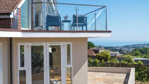 Ein modernes Haus mit einem Glasbalkon, einer Terrasse mit Steinböden und Blick auf das Meer.