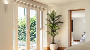 Ein helles Zimmer mit einer großen Schiebeglasdoor zum Balkon, einem Blumentopf und einem sichtbaren Bett im Hintergrund.
