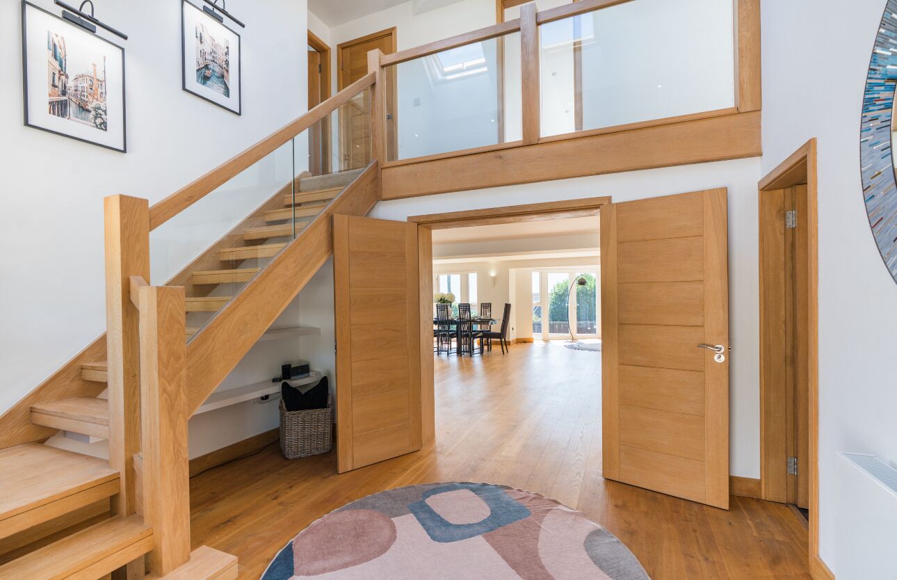 A spacious room with a wooden staircase, a dining area, and a large window.