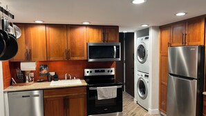 Une cuisine moderne dotée de meubles en bois, d’appareils électroménagers en acier inoxydable, notamment un four à micro-ondes, un four, un lave-vaisselle et un réfrigérateur, ainsi qu’une laveuse et une sécheuse intégrées.