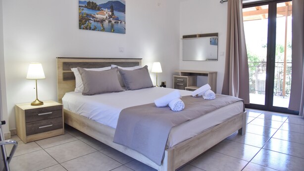A neatly made bed with a headboard, two bedside tables with lamps, a painting on the wall, a mirror, and a balcony with curtains.