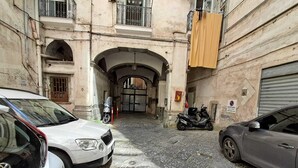 A narrow cobblestone street with parked cars and motorcycles, leading to a gated entrance with a sign. - 10elode House Spanish Neighborhoods (Napoli)