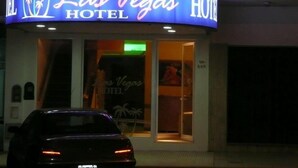 Het uiterlijk van Hotel Las Vegas, met een neonbord, een zichtbare ingang en een geparkeerde auto ervoor.