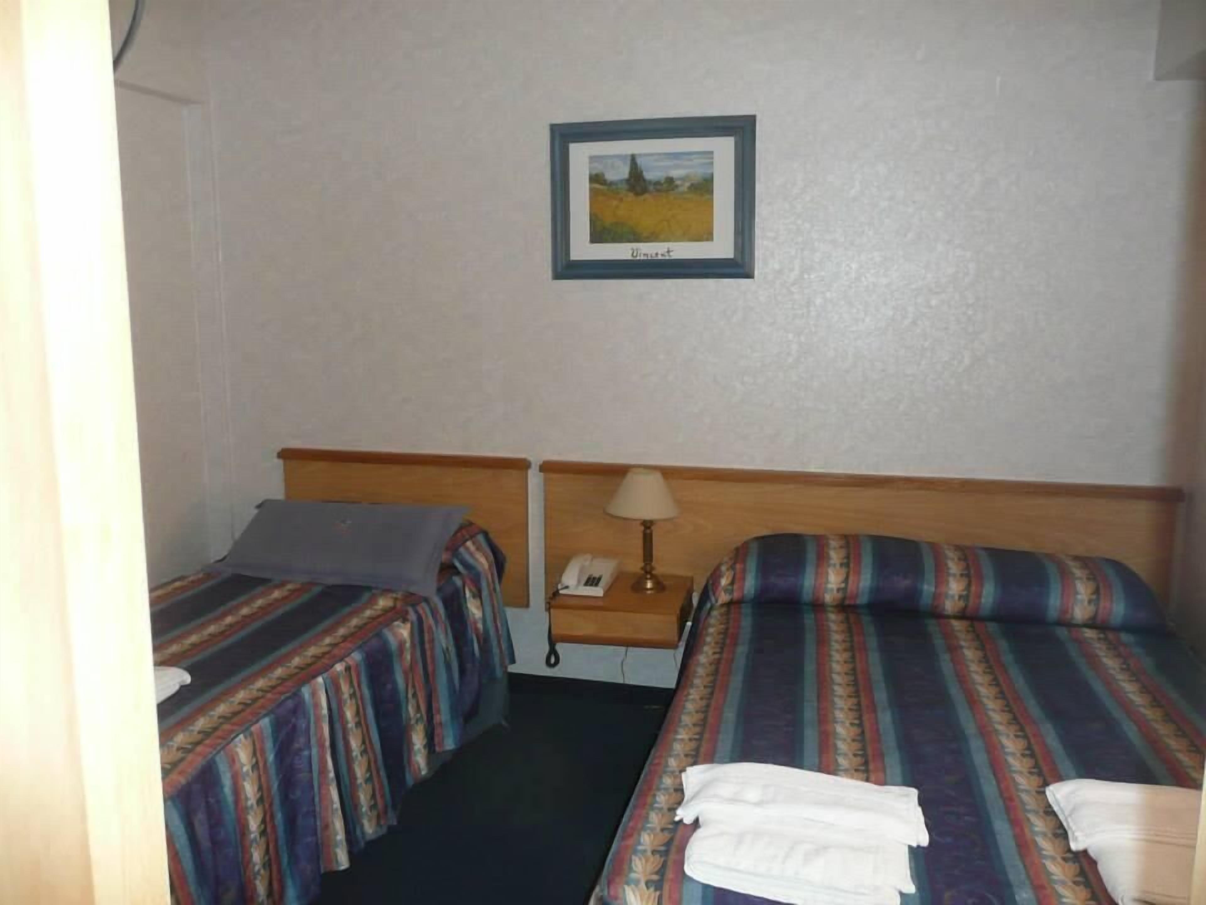 A hotel room with two beds, a nightstand with a lamp, and a framed picture on the wall.
