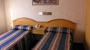 Een kamer met twee eenpersoonsbedden, een houten hoofdbord, een nachtkastje met een telefoon en een ingelijst kunstwerk aan de muur.