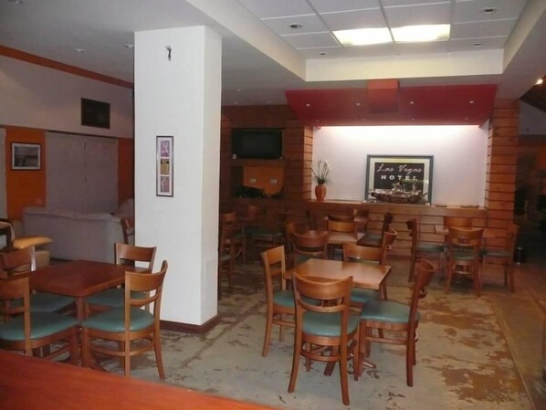 Un restaurant avec des tables et des chaises en bois, un pilier blanc et un tableau encadré au mur.