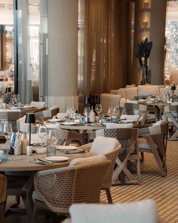 A restaurant with wicker furniture, round tables, and a patterned floor.