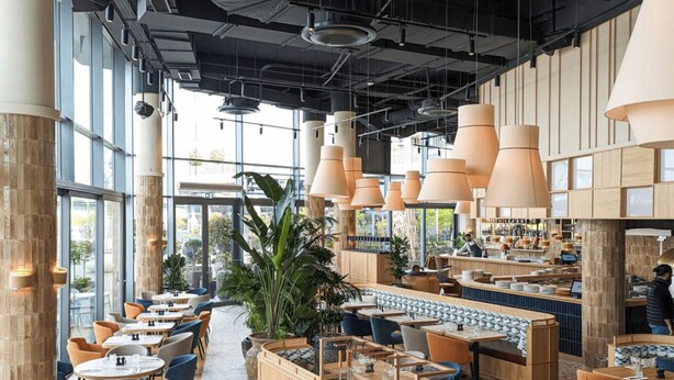 A modern restaurant with high ceilings, large pendant lights, and a mix of seating options including tables and booths.
