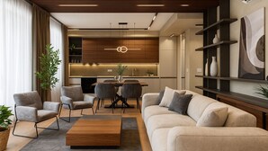 A modern living room with a sofa, armchairs, and a coffee table. There is a dining area with a table and chairs, and a kitchen in the background.