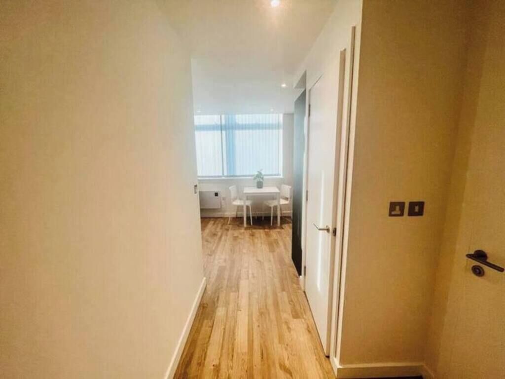 A narrow hallway with wooden flooring leading to a room with a white table and chairs.
