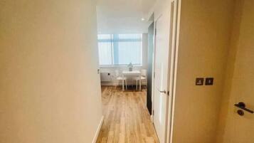A narrow hallway with wooden flooring leading to a room with a white table and chairs.