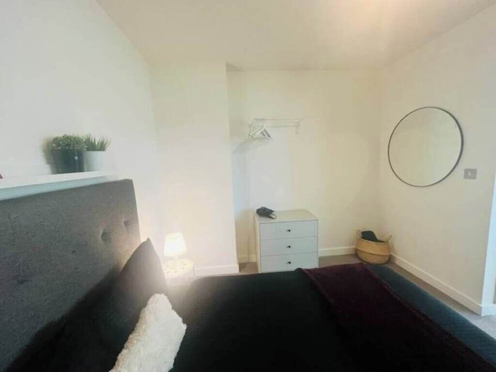 A bedroom with a bed, a bedside table, a small dresser, a mirror, and a potted plant.