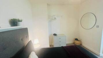 A bedroom with a bed, a bedside table, a small dresser, a mirror, and a potted plant.