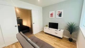 A modern living room with a sofa, a TV on a white cabinet, and a plant.