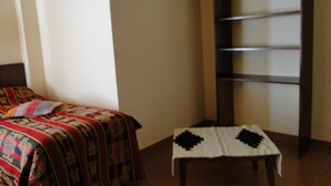 Une pièce avec un lit recouvert d’une couverture à motifs, une petite table recouverte d’une nappe blanche ornée d’un motif noir, et une échelle en bois appuyée contre le mur.