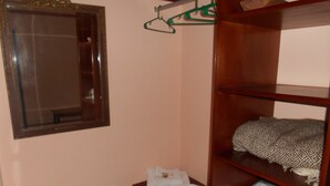 Une pièce avec une étagère en bois où sont pliés des serviettes, et un coussin à motifs. Un miroir avec un cadre doré est accroché au mur, et un cintre vert est visible.