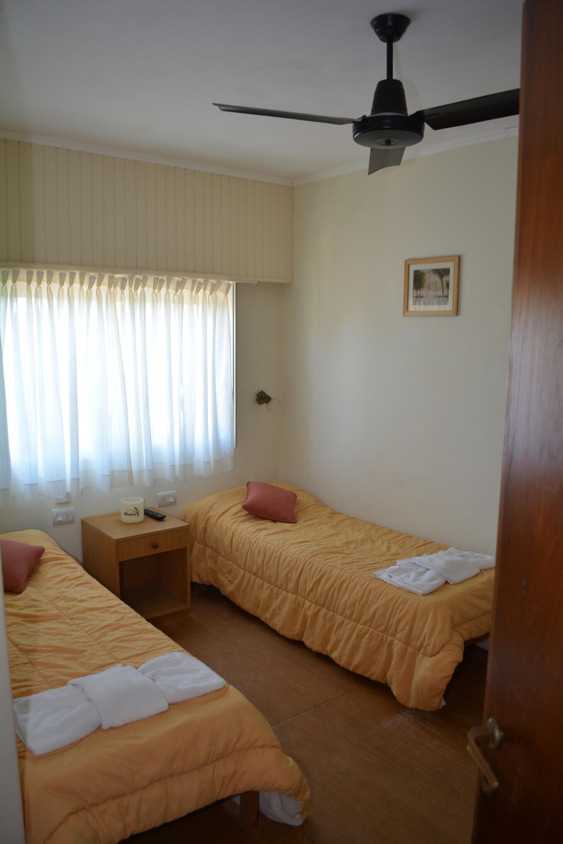 A hotel room with two beds, a ceiling fan, a nightstand, and a window with curtains.
