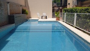 A rectangular swimming pool with clear blue water, surrounded by a white fence and potted plants.