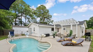 Un jardin avec une piscine, des chaises longues et un patio couvert.