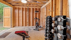 Une salle de sport avec des murs en bois, un ventilateur de plafond, un vélo d’exercice et des supports pour les poids.