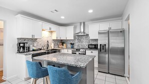 Une cuisine moderne avec des meubles blancs, un plan de travail en granit, des appareils électroménagers en acier inoxydable et des tabourets de bar bleus.