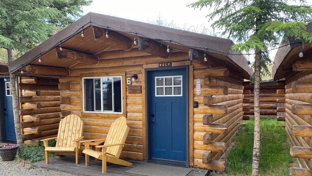 A log cabin with a blue door, two wooden chairs, and a welcome sign. - Wolf Cabin-Modern Comfort in the Last Frontier (For families or casual travelers) (Tok)