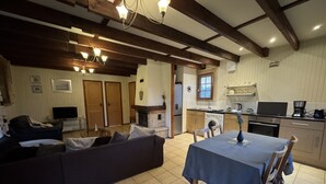 A living room with a sofa, a dining table with chairs, a fireplace, and a kitchen area with appliances. - Chalet in Aubigne-racan With Pool & Garden (Aubigne-Racan)