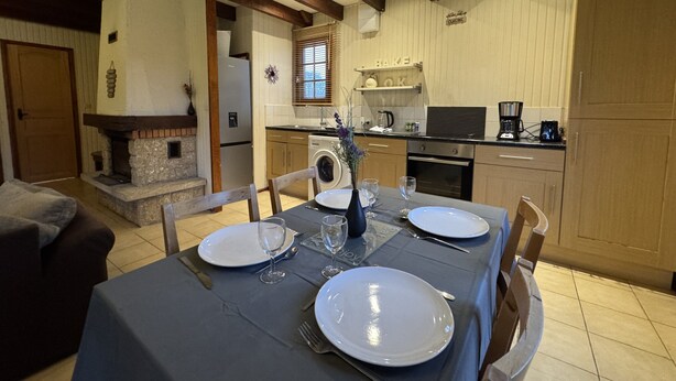A dining area with a table set for four, a fireplace, a kitchen with wooden cabinets, and a stone fireplace. - Chalet in Aubigne-racan With Pool & Garden (Aubigne-Racan)