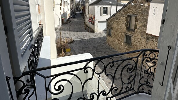 A narrow street with buildings on either side, a balcony with wrought iron railing, and a clear blue sky. - Villa in Le Mans Near Plantagenet City (Le Mans)
