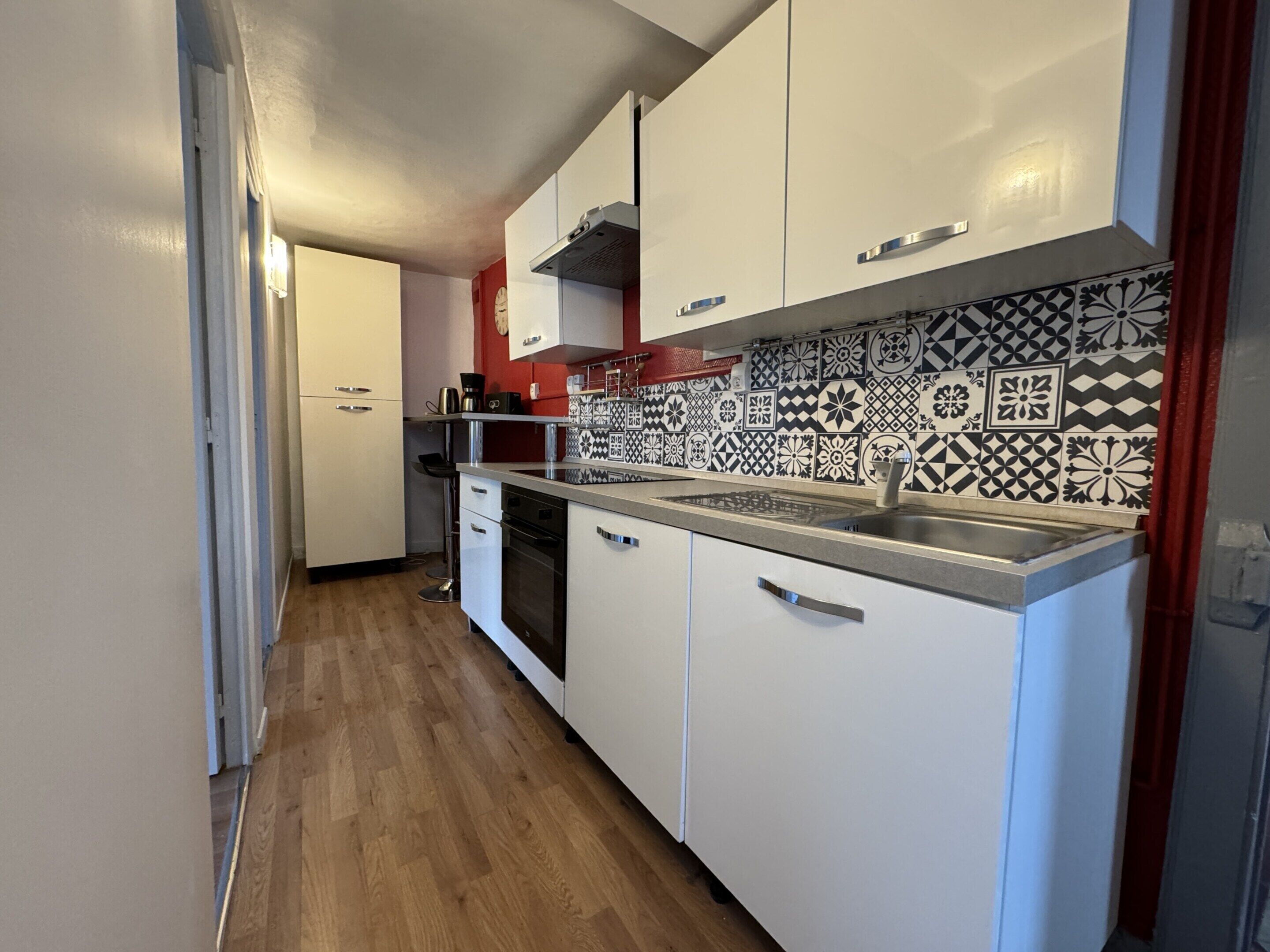 A kitchen with white cabinets, a patterned backsplash, and a wooden floor.