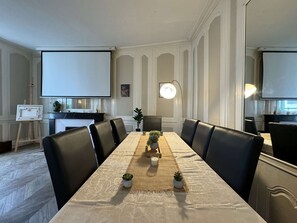Un salón de conferencias con una larga mesa, sillas de cuero negro, una pantalla de proyector y un caballete con una pintura.