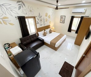 A hotel room with a bed, a sofa, a desk, and a flat-screen TV. - Jay and Jas Hotel (Tirupati)