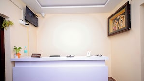 Een receptiebalie met een bordje met de tekst 'RECEPTION', een wandtelevisie, een beveiligingscamera en een kunstwerk in een lijst aan de muur.