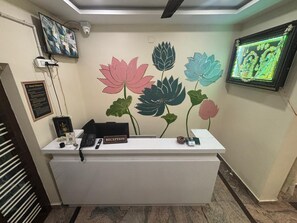 A reception desk with a 'RECEPTION' sign, a black telephone, a small plant, and a framed picture on the wall. - Jay and Jas Hotel (Tirupati)