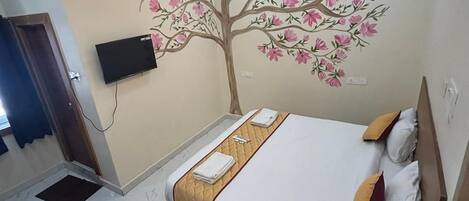 A bedroom with a bed, a ceiling fan, a wall-mounted TV, and a decorative tree mural.