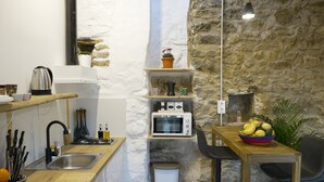 Una cocina compacta con pared de piedra, encimera de madera, pileta, pequeño basurero, microondas y una mesa con un bol de fruta.