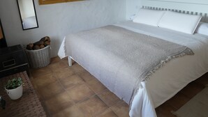Un dormitorio con una cama, una ventana de madera, un espejo y una pared de piedra.