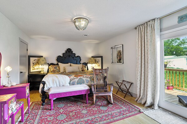 A bedroom with a large bed, a chair, a bench, and a view of the outdoors.