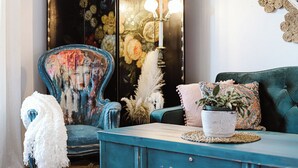 Ein blaues Sofa mit weißer Decke, ein floraler Sessel und ein Blumentopf auf einem blauen Schrank.