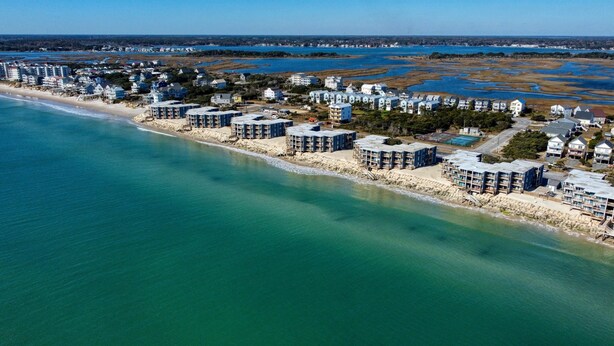 Vista aérea de una zona residencial costera con propiedades frente a la playa, incluyendo edificios de varios pisos y casas junto a la playa.