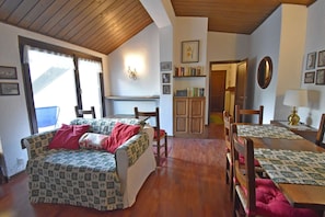 Um quarto acolhedor com teto de madeira, um sofá com roupa de cama estampada, uma mesa de jantar com um jogo americano e uma estante de livros.
