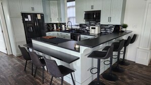 A modern kitchen with white cabinetry, a black countertop island with bar stools, and a stainless steel refrigerator. - Cozy Waterfront Country Home w/game room. Close to all amenities! (Lot 19)