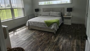 A bedroom with a bed, two bedside tables, a window, and a view of a green lawn. - Cozy Waterfront Country Home w/game room. Close to all amenities! (Lot 19)