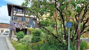 A traditional building with a balcony, surrounded by lush greenery and purple flowering vines. - Gîte Lisière d'Argonne (Passavant-en-Argonne)
