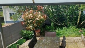 An outdoor patio with a table and chairs, surrounded by greenery and a view of a building. - Gîte Lisière d'Argonne (Passavant-en-Argonne)