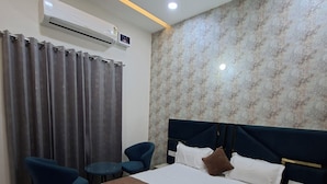 A hotel room with a bed, bedside table, chair, and an air conditioning unit. - Wishotel Xpress Hotel Crown Classic Villa (Ludhiana)