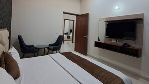A modern hotel room with a large bed, a desk, two chairs, a ceiling fan, and a TV mounted on the wall. - Wishotel Xpress Hotel Crown Classic Villa (Ludhiana)