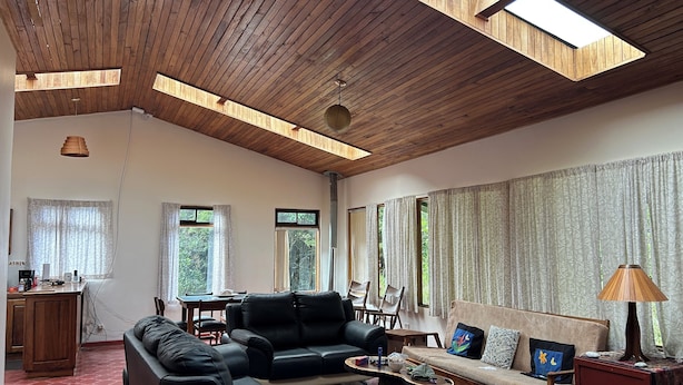 A spacious living room with a high wooden ceiling, a sofa, a coffee table, and a dining area with a table and chairs.